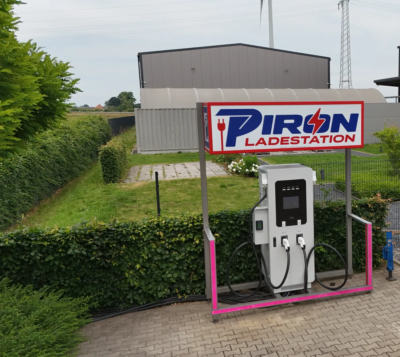 De PIRON snellader met twee CCS-kabels onder het rood-blauwe PIRON-bord in Kleve