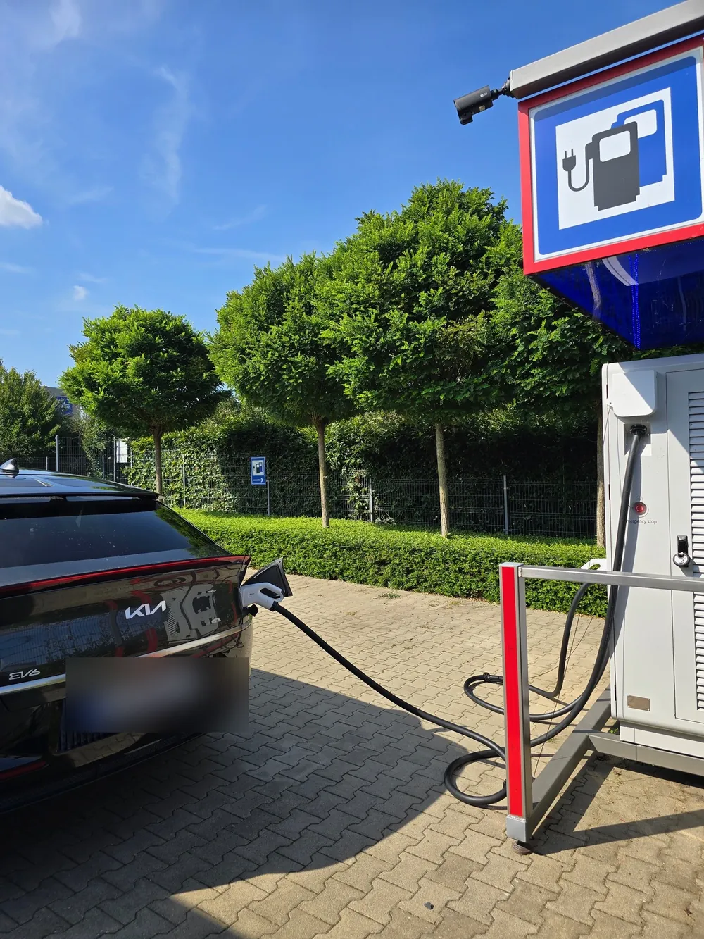 Schwarzer Kia EV6 lädt am CCS-Kabel der PIRON-Säule, darüber das blaue Ladesäulen-Schild mit der Kamera